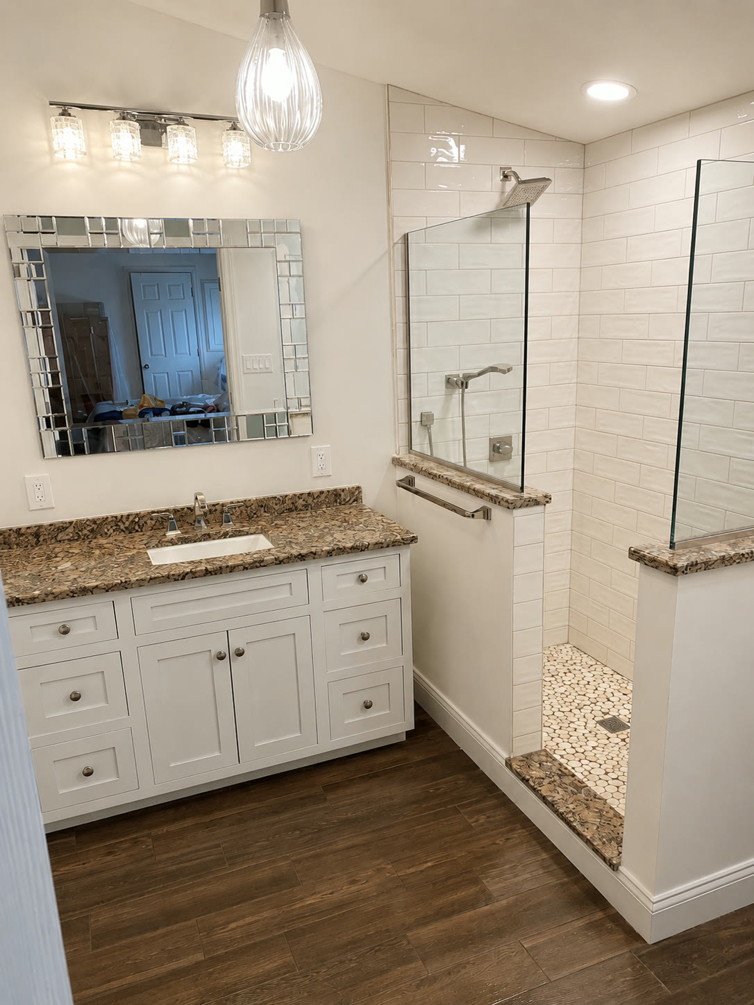 Walk-in shower with glass half walls and pebble floor beside a white vanity with a granite countertop