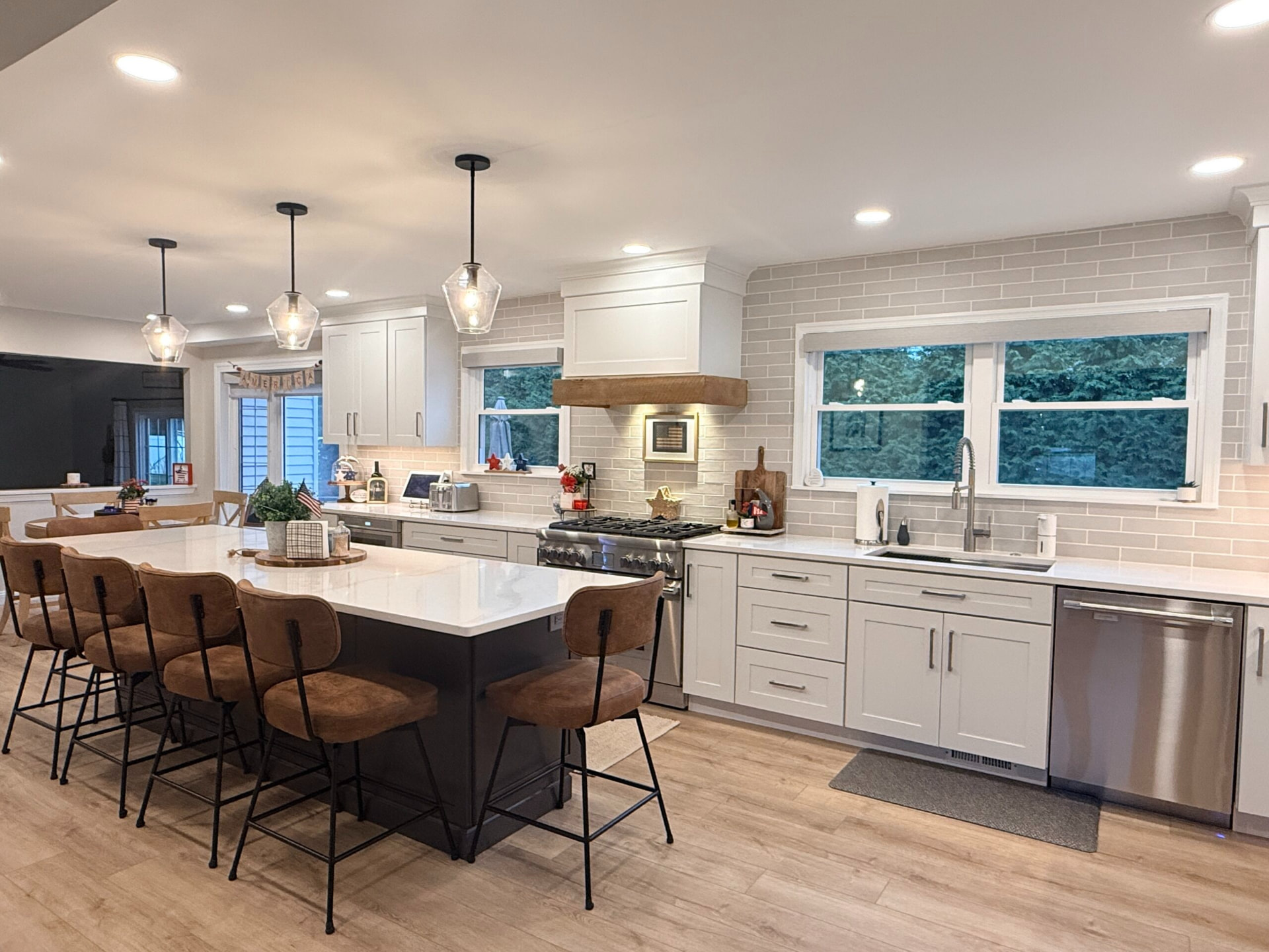 Open-concept kitchen remodel with a dark island base, wood mantle range hood, and white subway tile