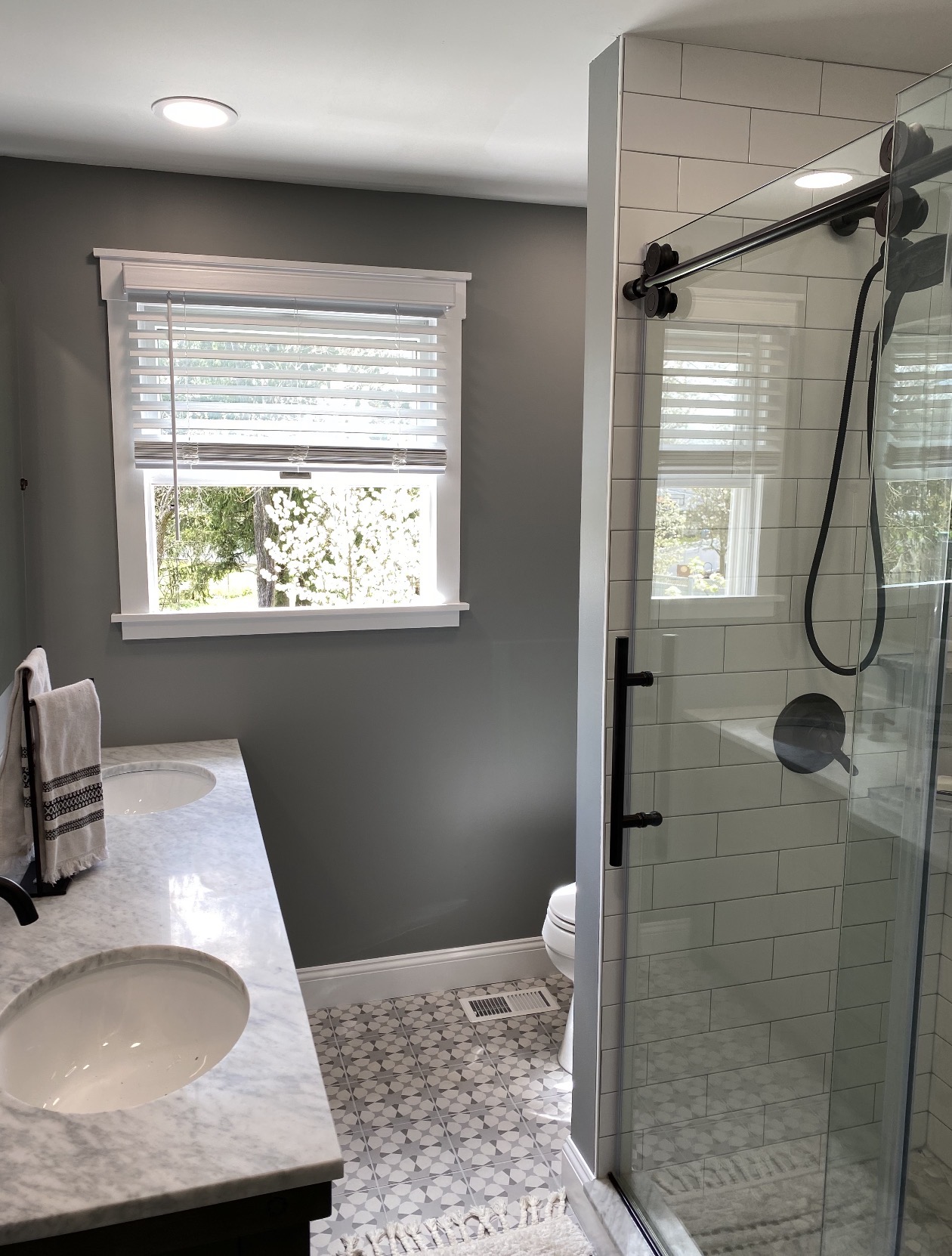 Bathroom with a double vanity, black-framed glass shower with sliding barn door, and patterned tile floor