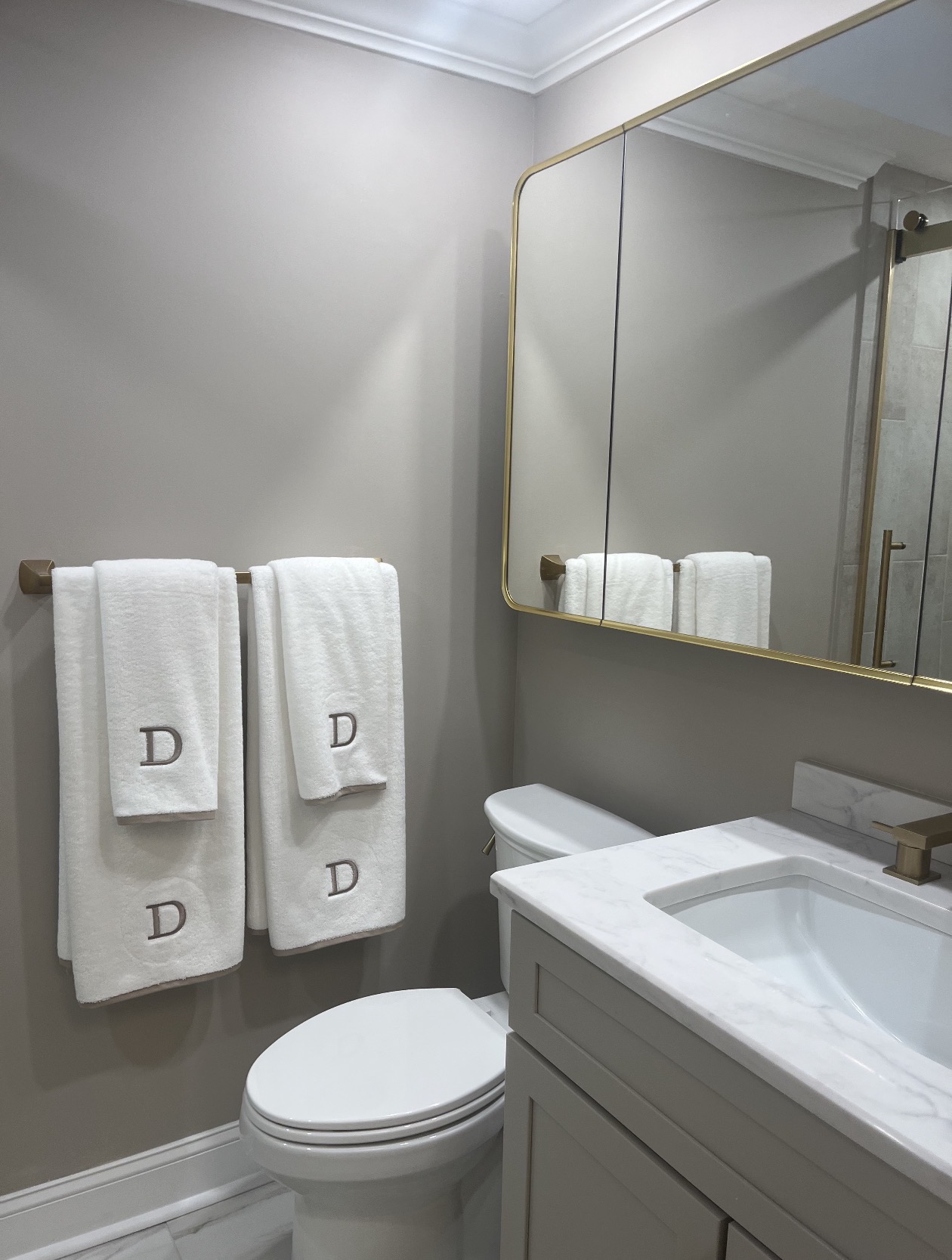 Bathroom vanity with a marble countertop, brushed brass mirror, and matching towel bar