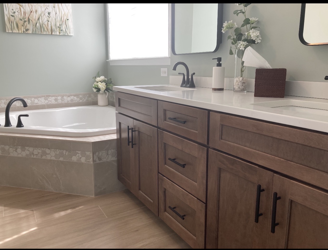 Finished bathroom with a wood double-sink vanity, corner soaking tub, hexagonal tile border, and pale green walls